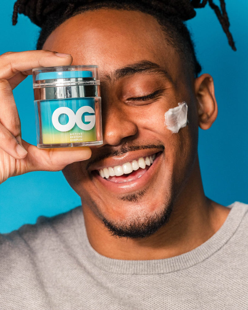 Man holding Active Restore Cream jar over one eye, cream on his cheek